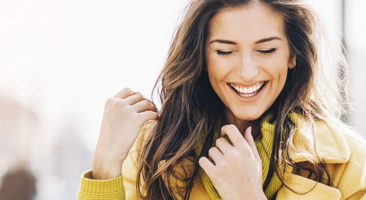 Beautiful young woman smiling and walking outdoors in the city, with sunlight and copy space